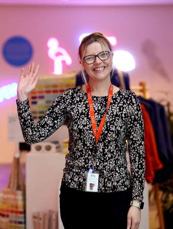 A photograph of a member of Tate Liverpool staff standing and smiling whilst waving at the camera