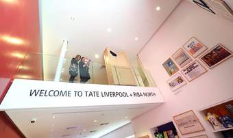 A photograph of two visitors standing by a glass-panelled balcony reading a booklet