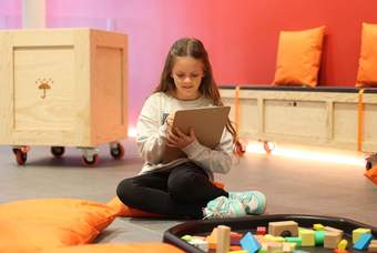 A photograph of a little girl sat drawing on a clipboard