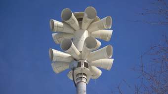 A large white speaker device against a bright blue sky