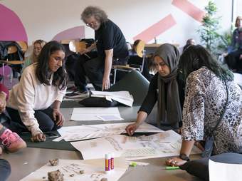 A group of people sit together looking at some written phrases arranged on a large sheet of paper.