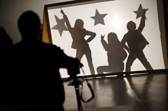 A photograph showing the shadows of three children posing behind a piece of material that's lit from a light behind.