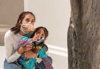 a parent and a child point and look at a statue in the gallery.