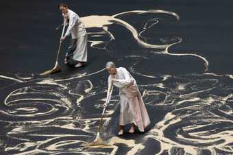 two performers sweeping rice on a dark floor