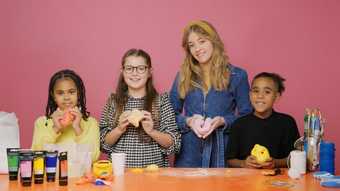 An adult and three children holding sculptures they have made at a table with art supplies