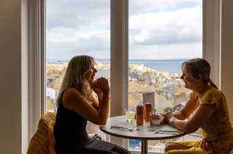 Two people sitting at a table with drinks next to a window overlooking the town and the sea