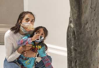 parent and child wearing masks point and look at a sculpture in the gallery