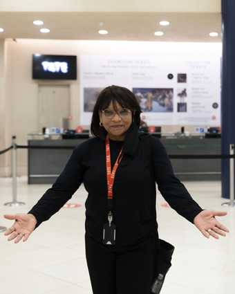 a visitor assitant stands with arms outstretched in a foyer 