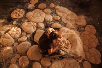 Looking from above down at a woman sat on the floor with piles of wet sand around her in different shapes.